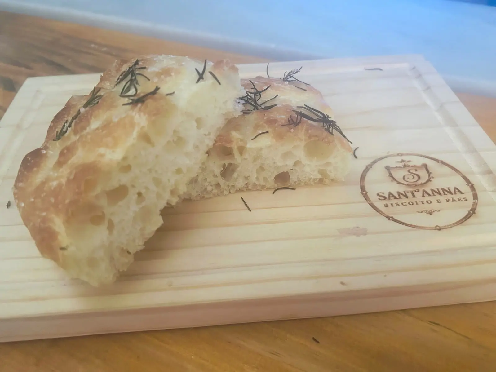 Focaccia tradicional de sal e alecrim partida ao meio, mostrando o miolo aerado, sobre a tábua da Sant'Anna