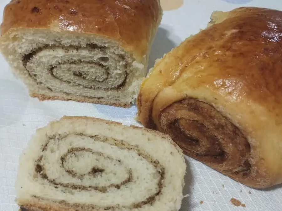 Pão doce de canela: Massa doce enrolada com canela, assada em forma alta. Cada fatia abre em espiral.